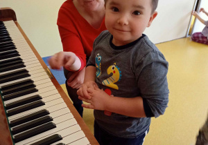 Chłopiec próbuje grać na pianinie.
